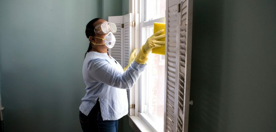 woman in face mask cleaning windows