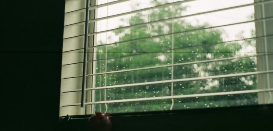 Open blinds over a storm window with all-season Climate Seal Window Inserts during a rainstorm
