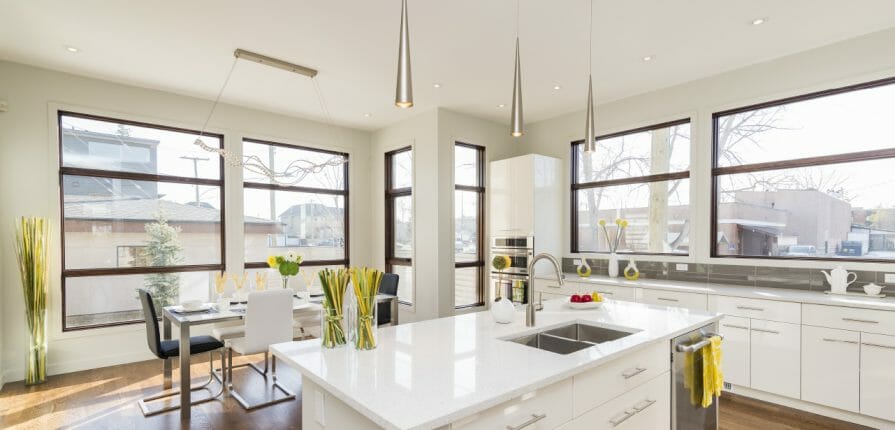 Photo of a bright, white and clean kitchen. Windows along two walls let in lots of natural daytime light.